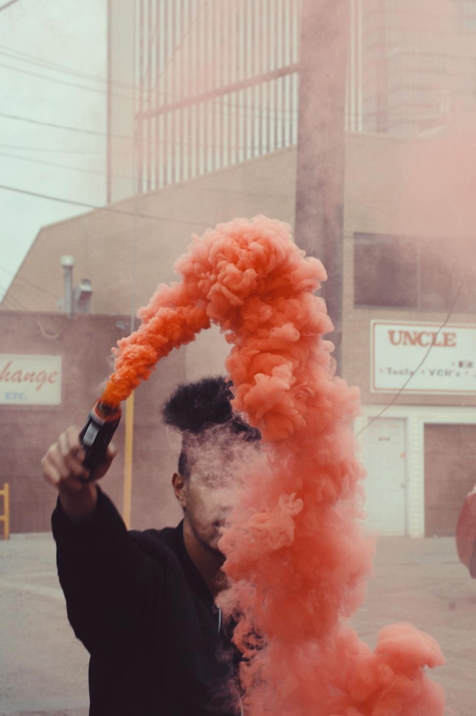 Free Image of Person igniting red smoke flare in city 