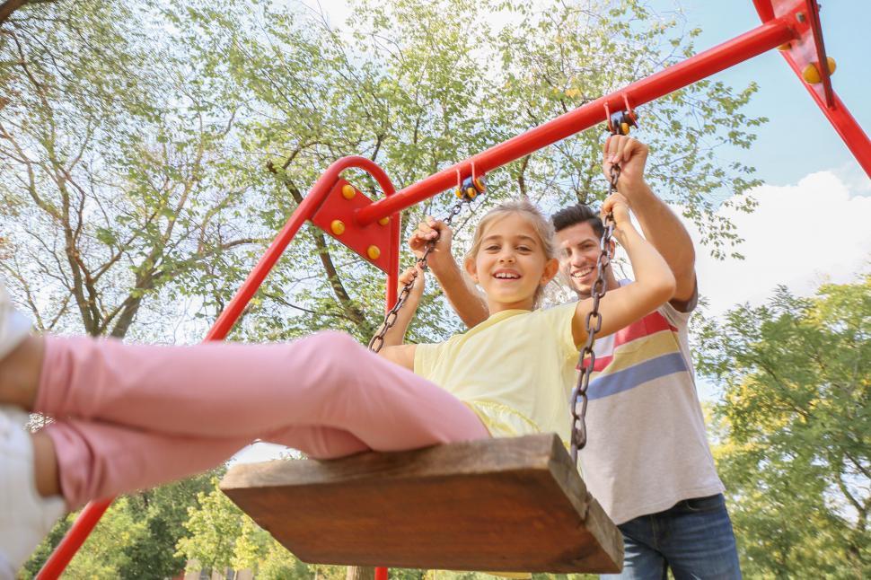 Free Image of Girl smiling on a swing with dad behind 