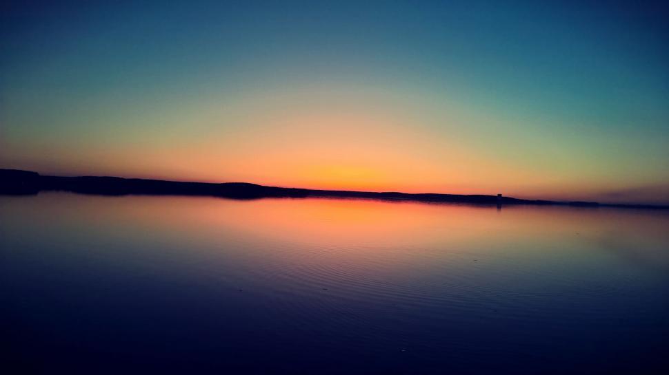 Free Image of Silhouette sunset with gradient sky over calm waters 