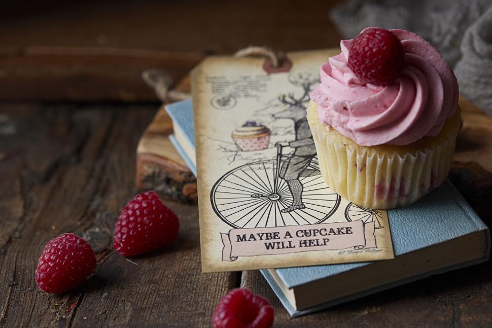 Free Image of Cupcake with pink frosting beside books 