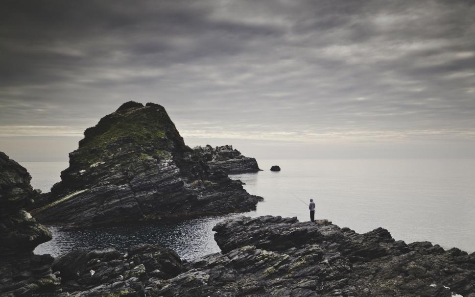 Free Image of Solitary figure fishing by rocky seaside 