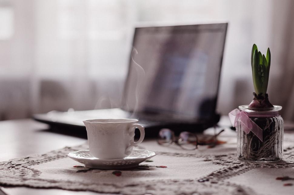 Free Image of Steaming coffee cup by laptop on table 