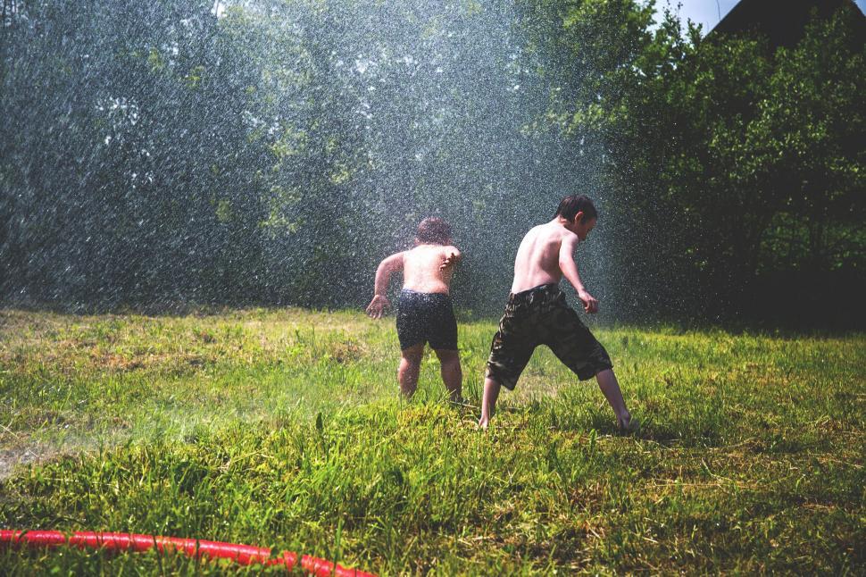 Free Image of Kids playing in water sprinklers on lawn 
