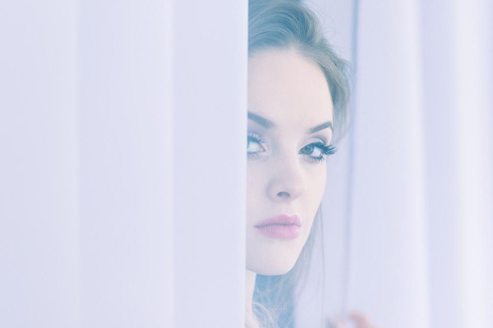 Free Image of Woman peering through white blinds 