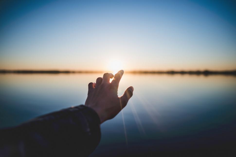 Free Image of Hand reaching towards sun above lake 
