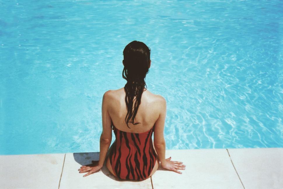 Free Image of Woman relaxing by the pool in a tiger print swimsuit 