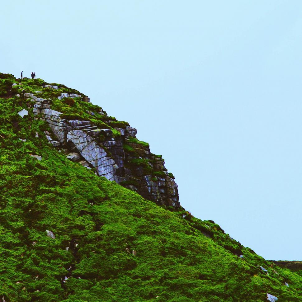 Free Image of Solitary hikers on the edge of a lush green cliff 