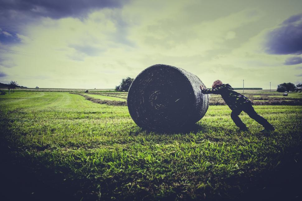 Free Image of Man pushing a large rolled hay bale 