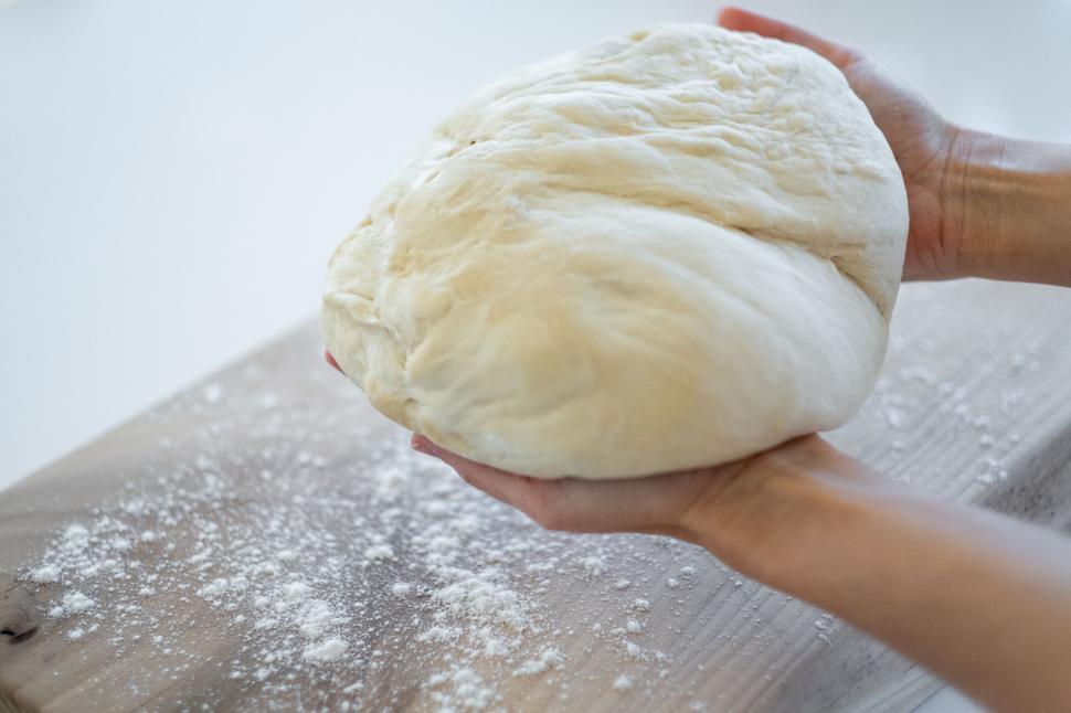 Free Image of Hands holding fresh dough on board 