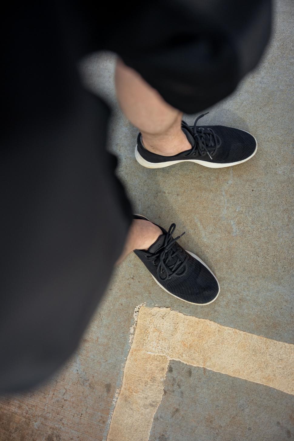Free Image of Man s feet in black sneakers on pavement 