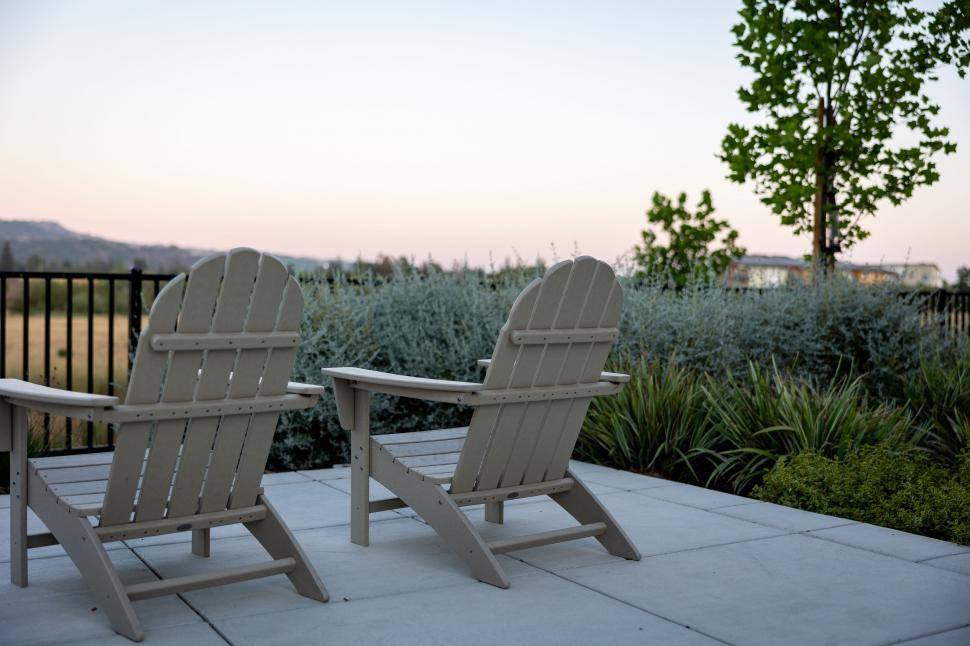 Free Image of Two Adirondack chairs facing a plush garden 
