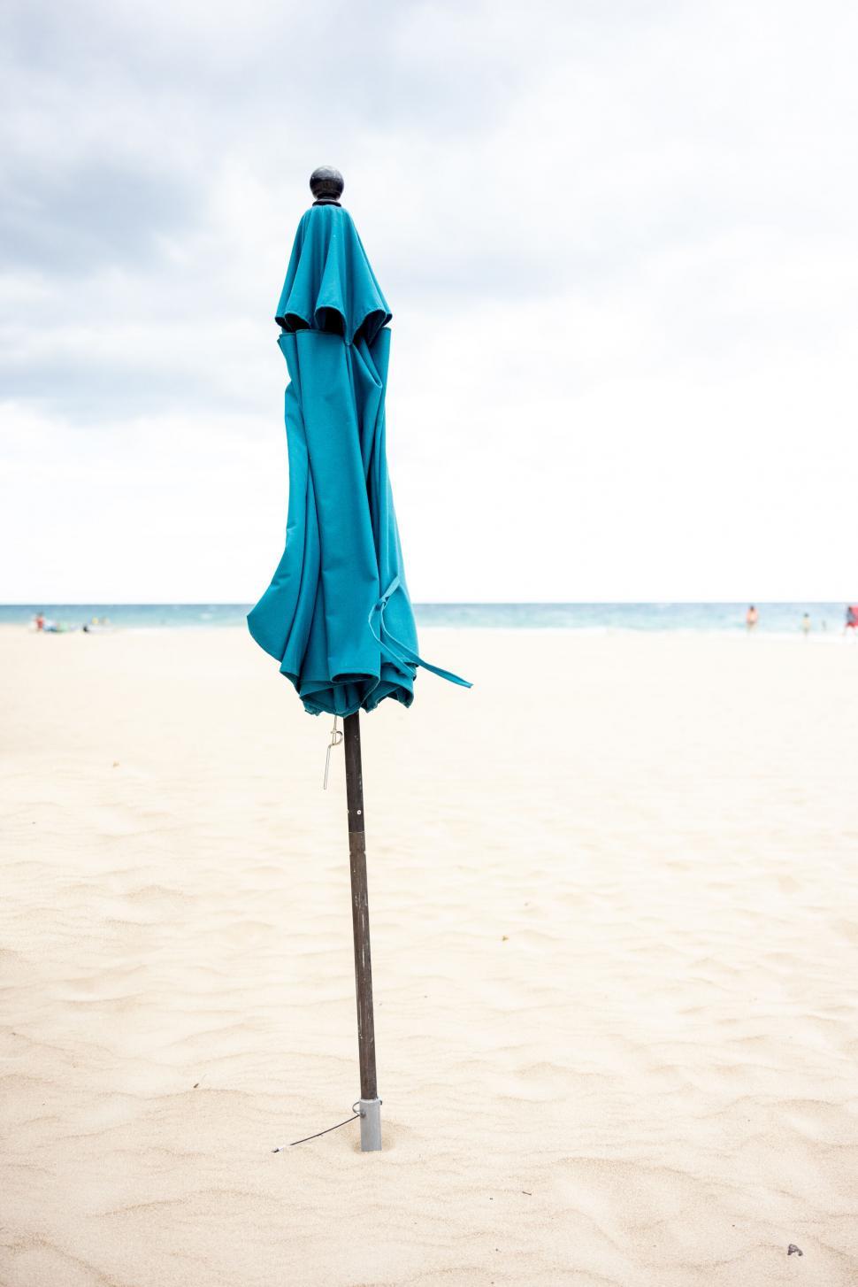 Free Image of Closed blue beach umbrella on sandy shore 