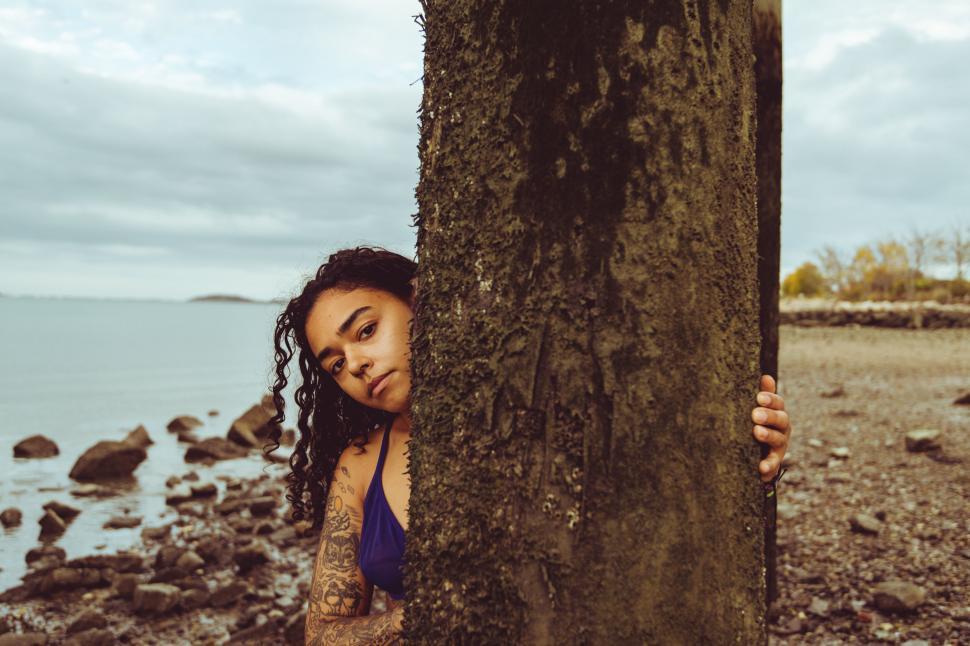 Free Image of Tattooed woman hiding behind a tree 