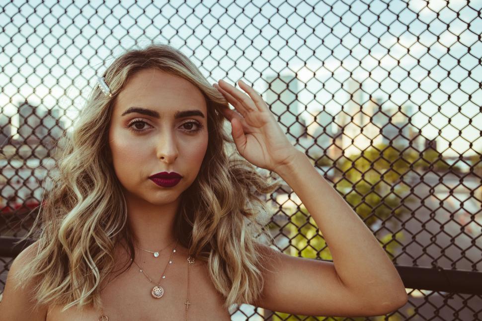 Free Image of Woman by fence at sunset with strong gaze 