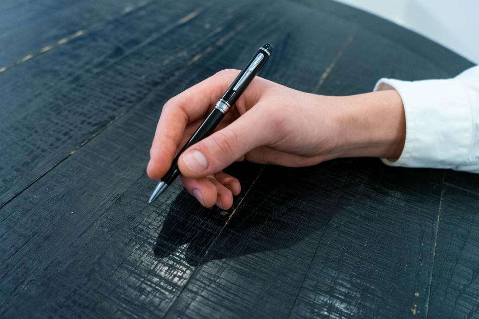 Free Image of Hand holding a pen ready to write on a table 