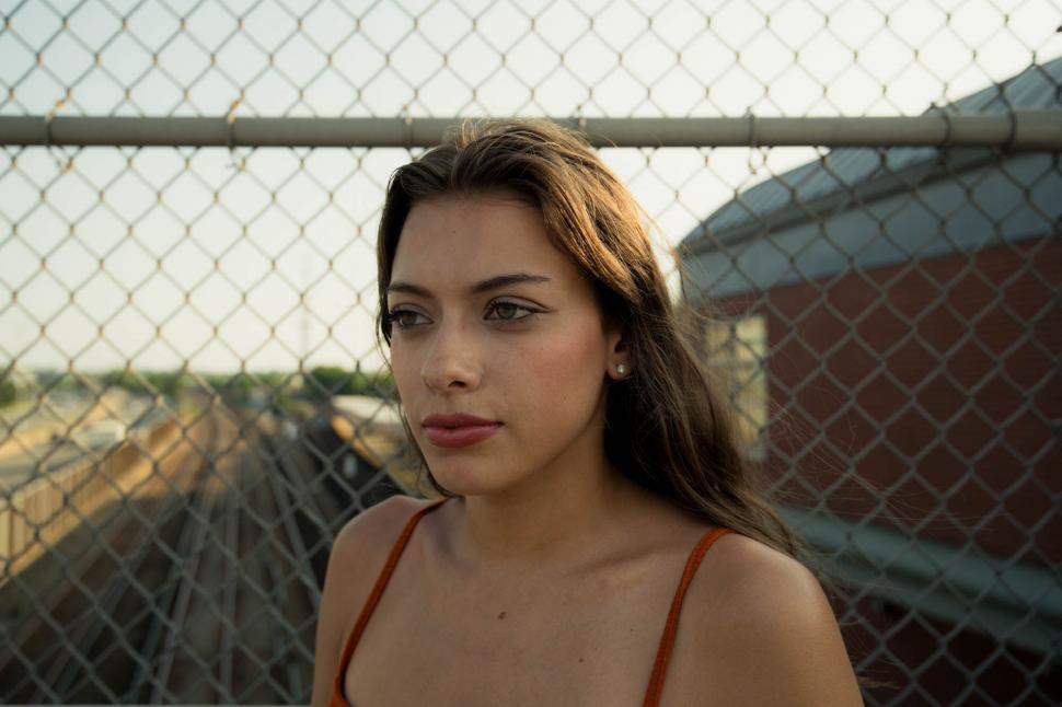 Free Image of Woman with pensive look by chain-link fence 