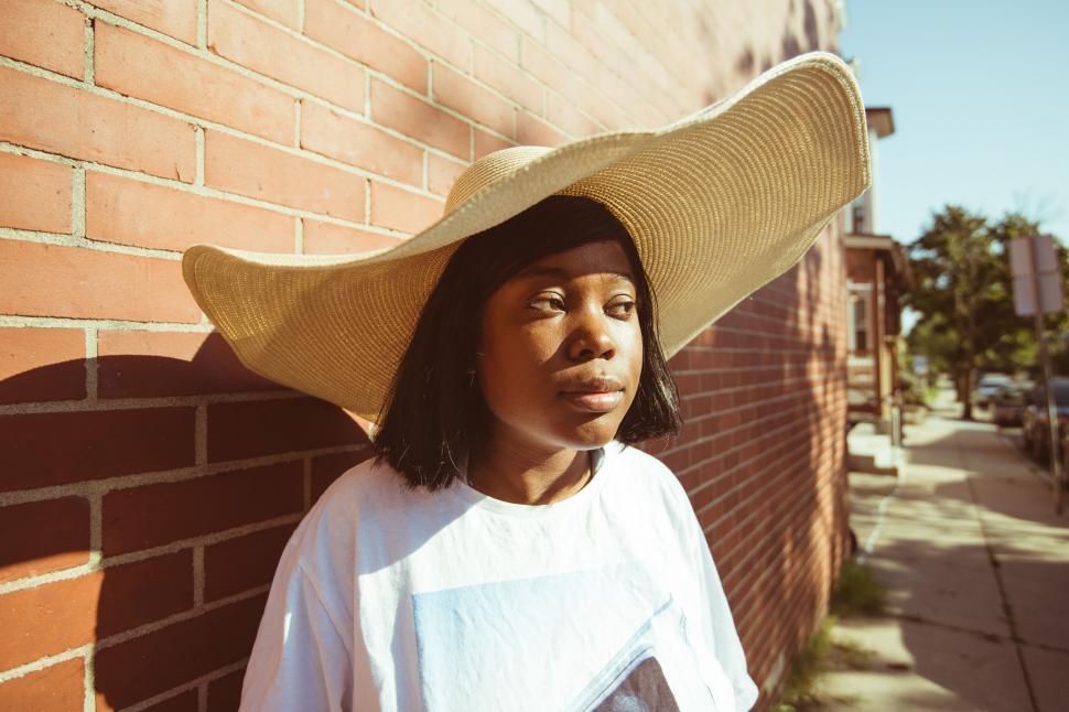 Free Image of Woman in oversized sunhat leaning on wall 