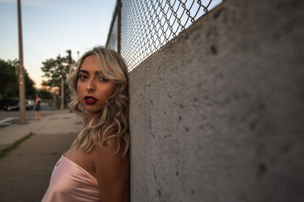 Free Image of Woman standing beside fence with urban backdrop 