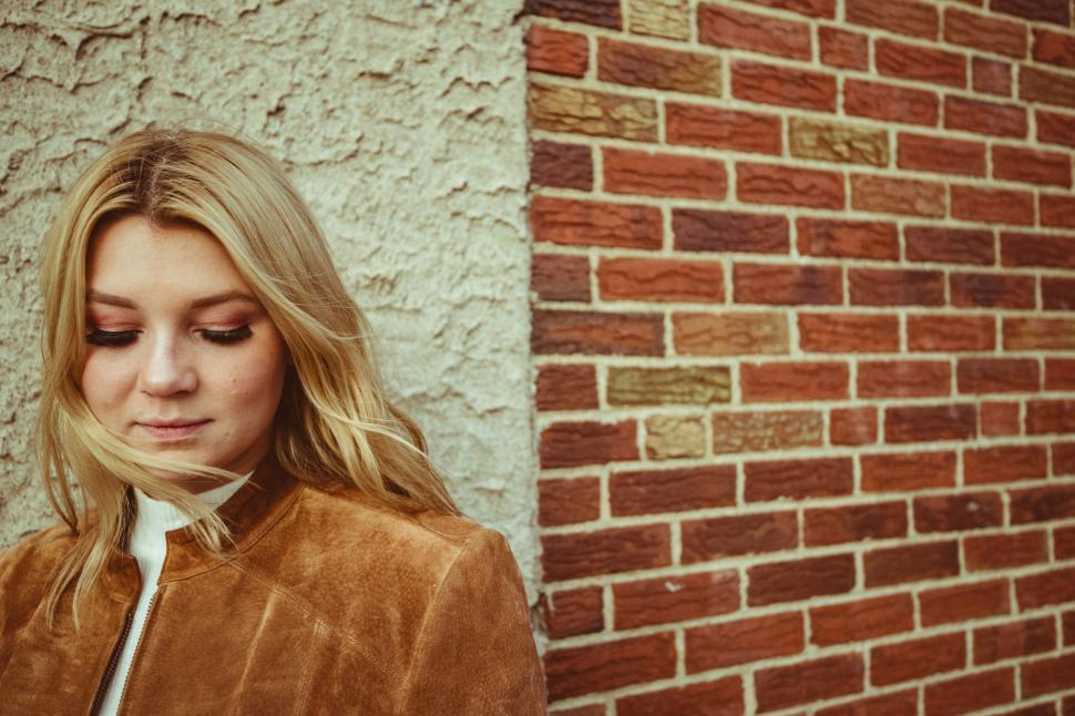 Free Image of Woman with eyes down near brick wall 