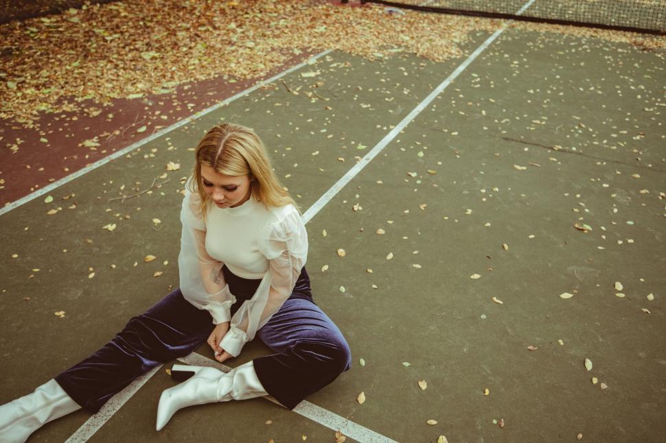 Free Image of Woman sitting on tennis court with autumn leaves 