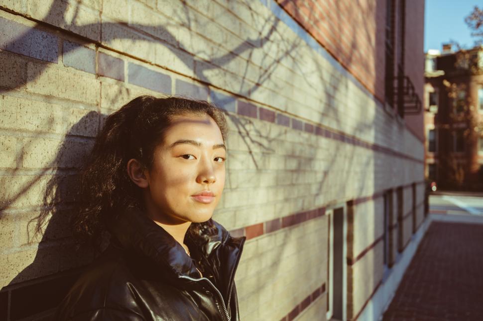 Free Image of Young woman in sunlight by brick wall 
