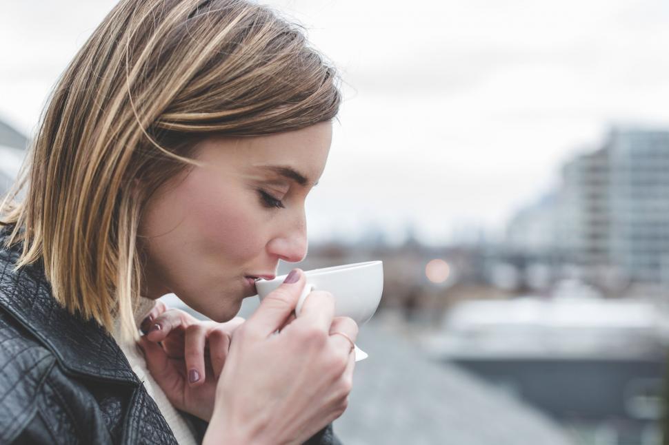 Free Image of Woman holding cup obscuring face with city view 