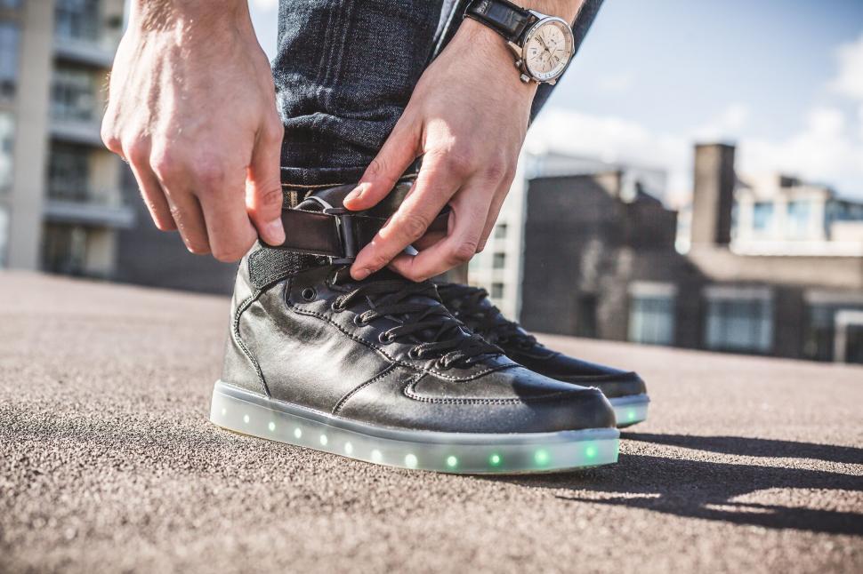 Free Image of Man tying his illuminated sneakers on street 