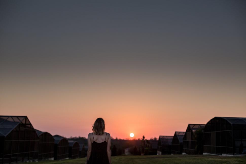 Free Image of Woman watching sunset over greenhouses 