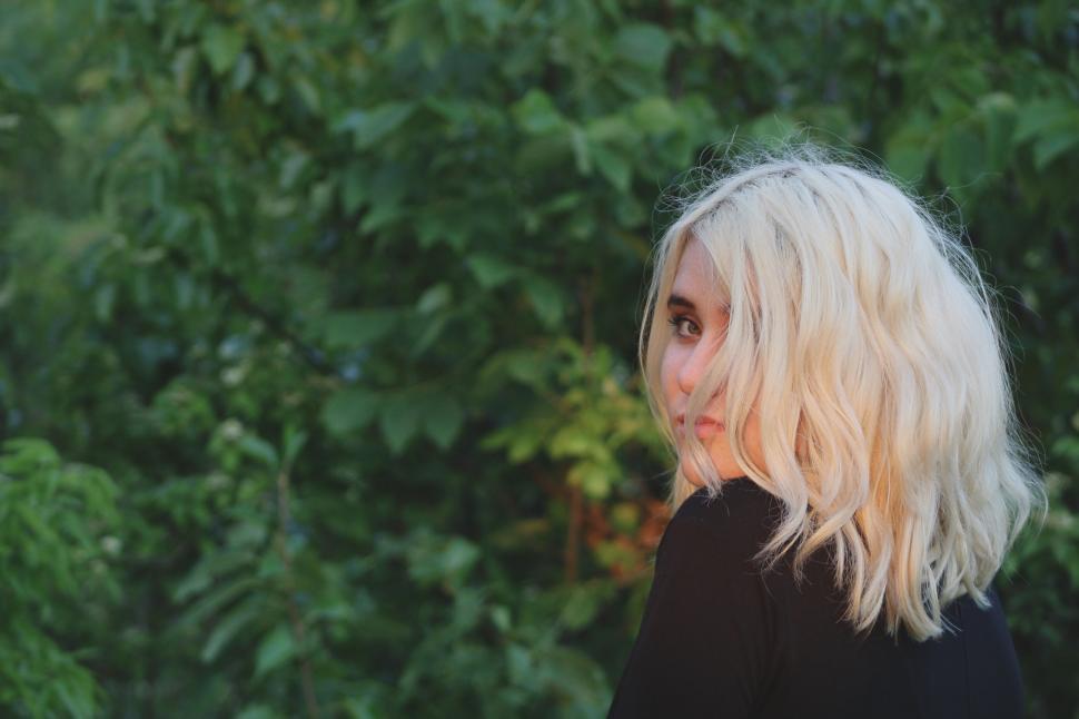Free Image of Blonde woman standing in front of green foliage 