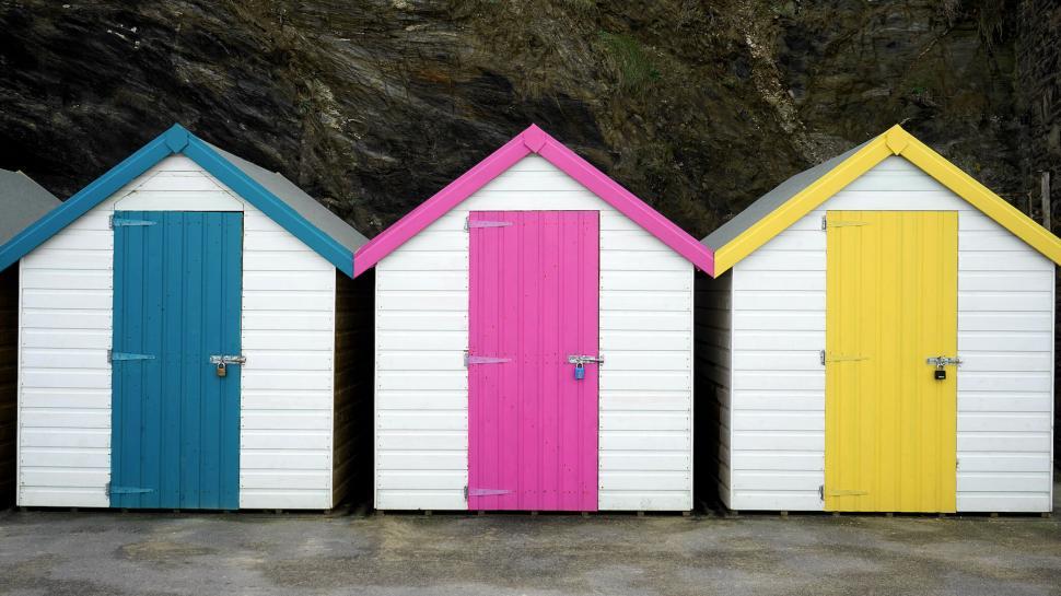 Free Image of Colorful beach huts against a rocky backdrop 