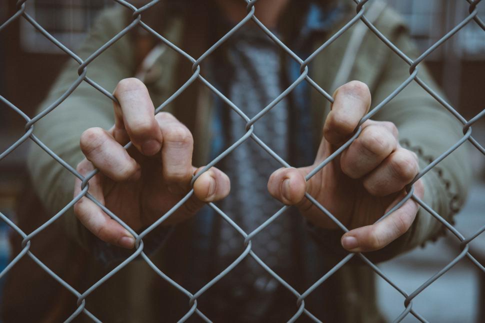 Free Image of Hands gripping a chain-link fence tightly 