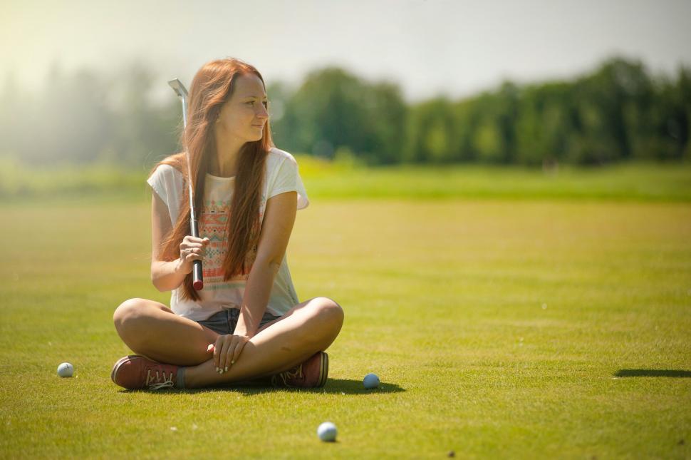 Free Image of Girl sitting in a field holding a baseball bat 