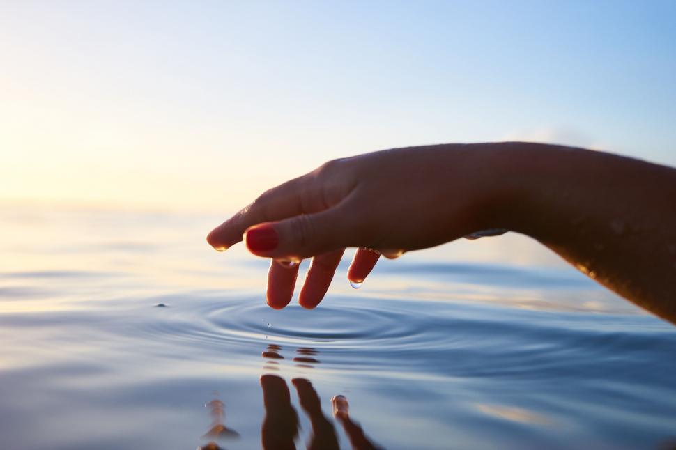 Free Image of Hand touching water surface at sunset 