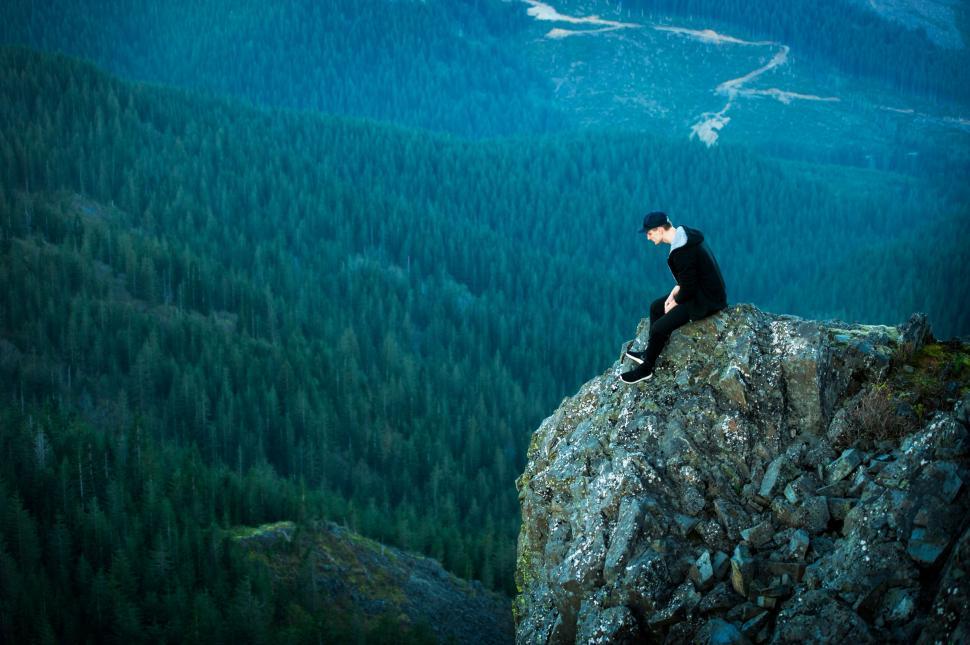 Free Image of Man perched on cliff overlooking forest 