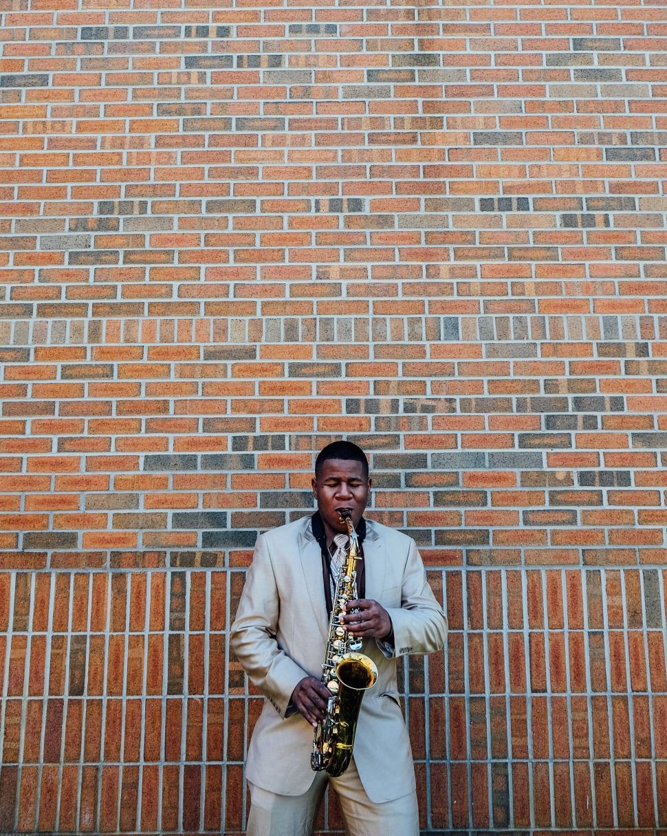 Free Image of Man playing saxophone against brick wall 