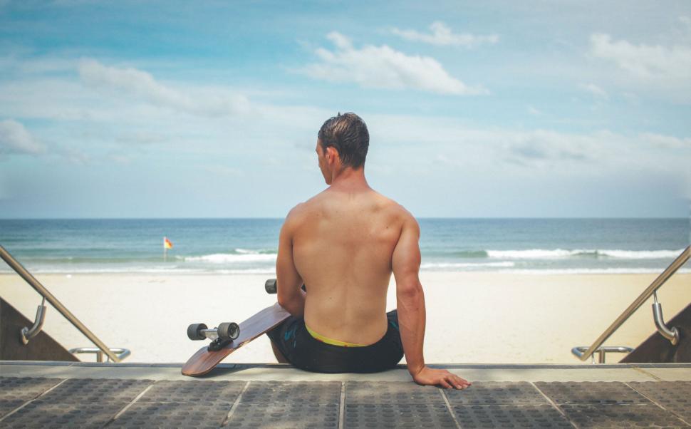 Free Image of Man sitting with skateboard looking at the beach 