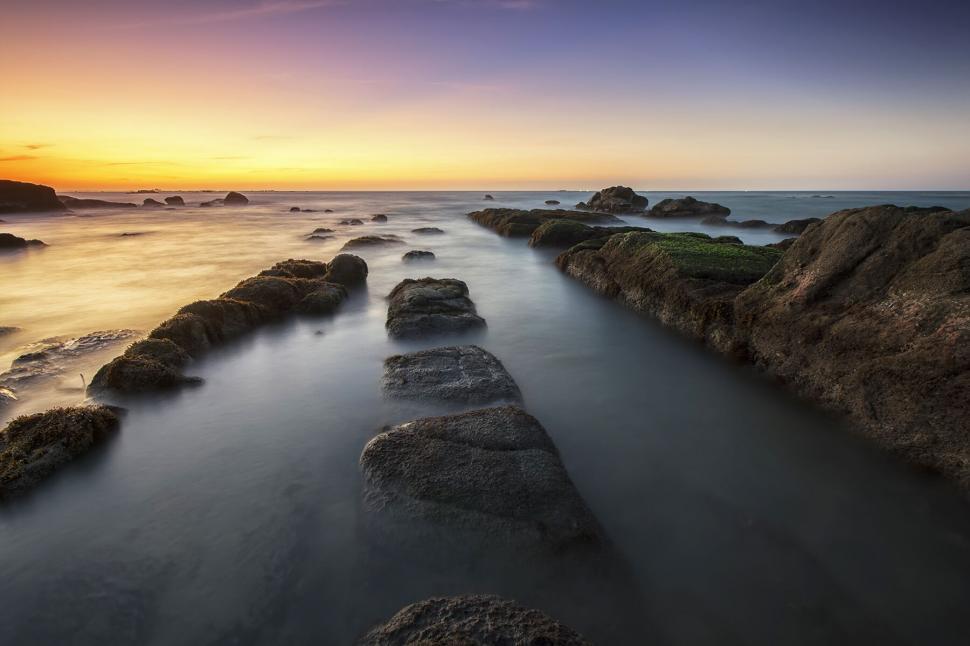 Free Image of Serene sunset with smooth rock formations in sea 