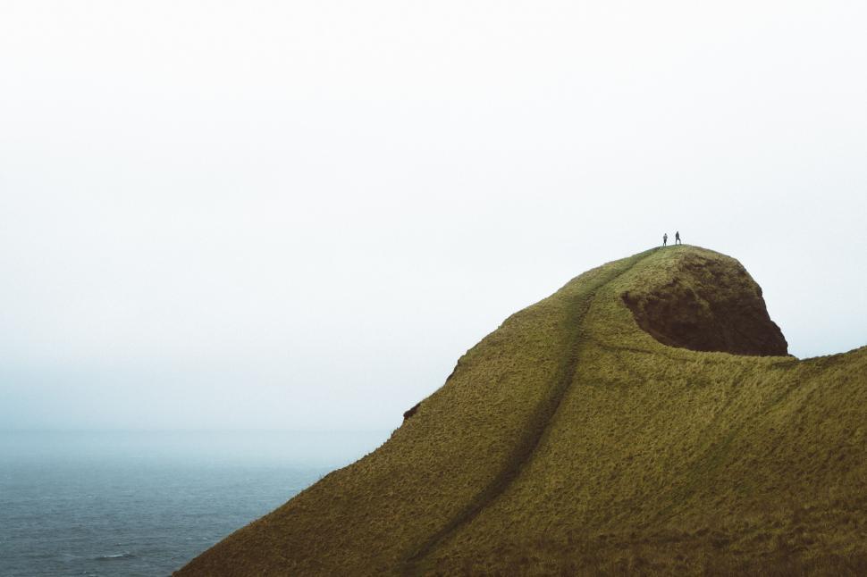 Free Image of Two people on top of a lush green coastal hill 