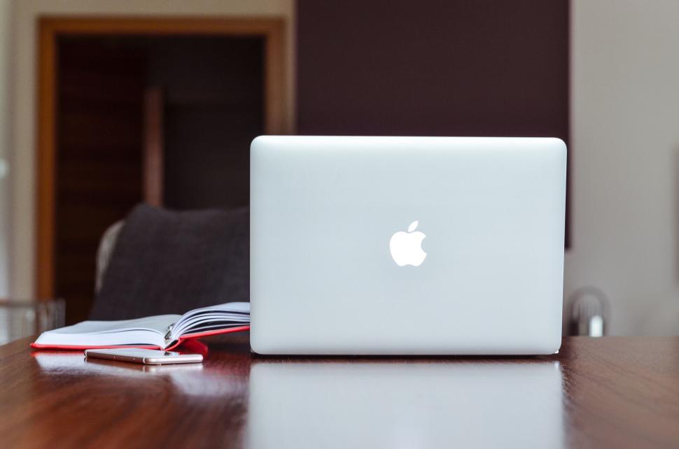 Free Image of Laptop with Apple logo on wooden table, book aside 