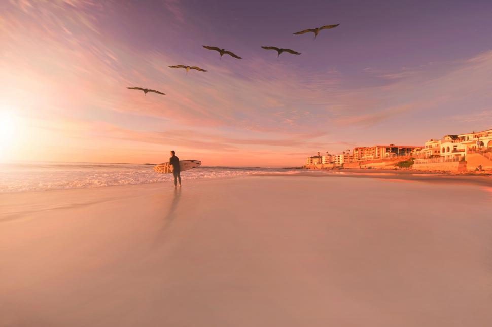 Free Image of Surfer walking on beach at colorful sunset 