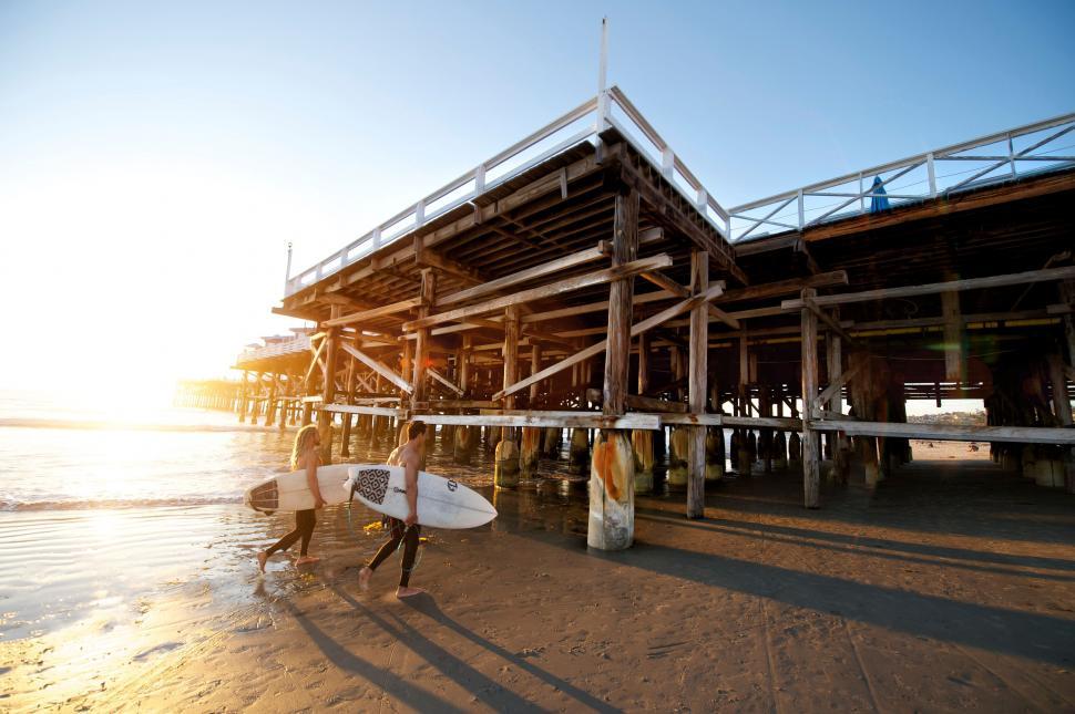 Free Image of Surfers heading to the pier at sunset 