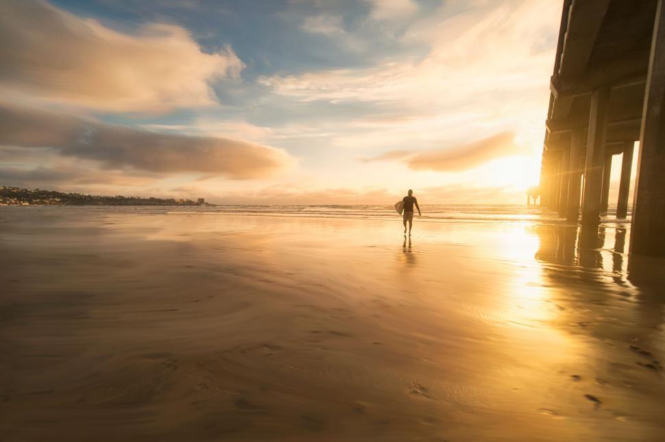 Free Image of Surfer walking under pier at sunset 