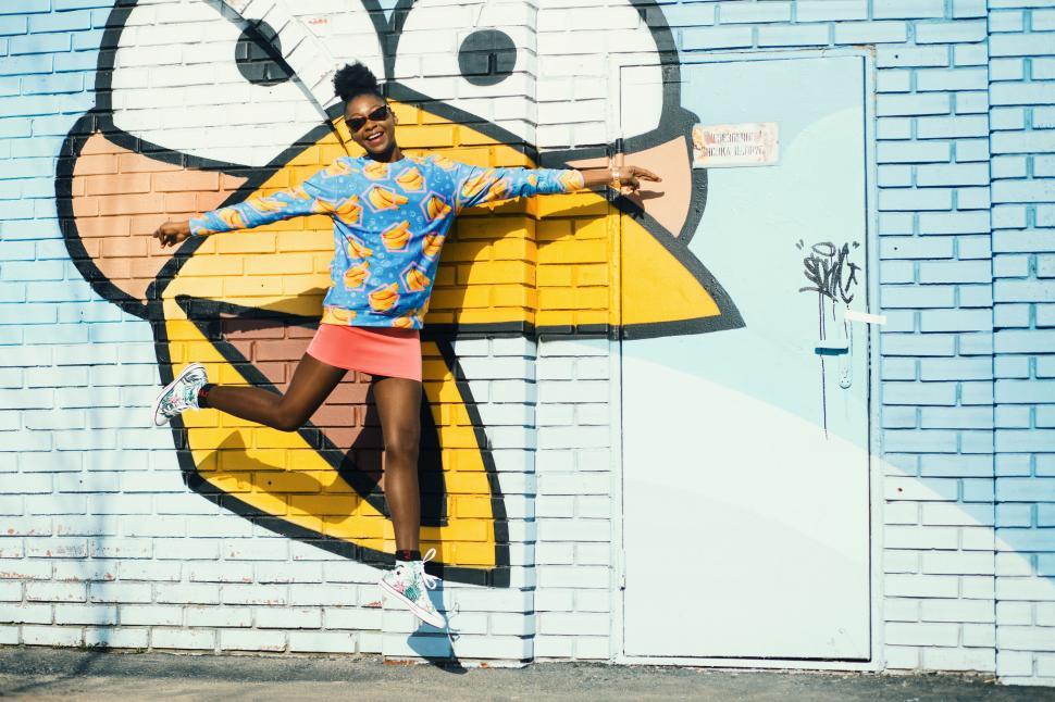 Free Image of Woman jumping in front of graffiti wall 