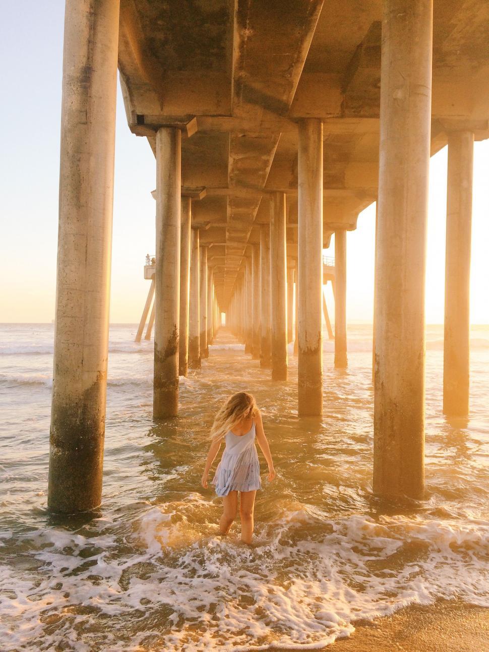 Free Image of Girl walking under pier with sunset light 