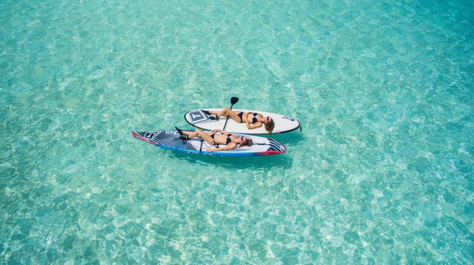 Free Image of Man and woman sunbathing on paddleboards 
