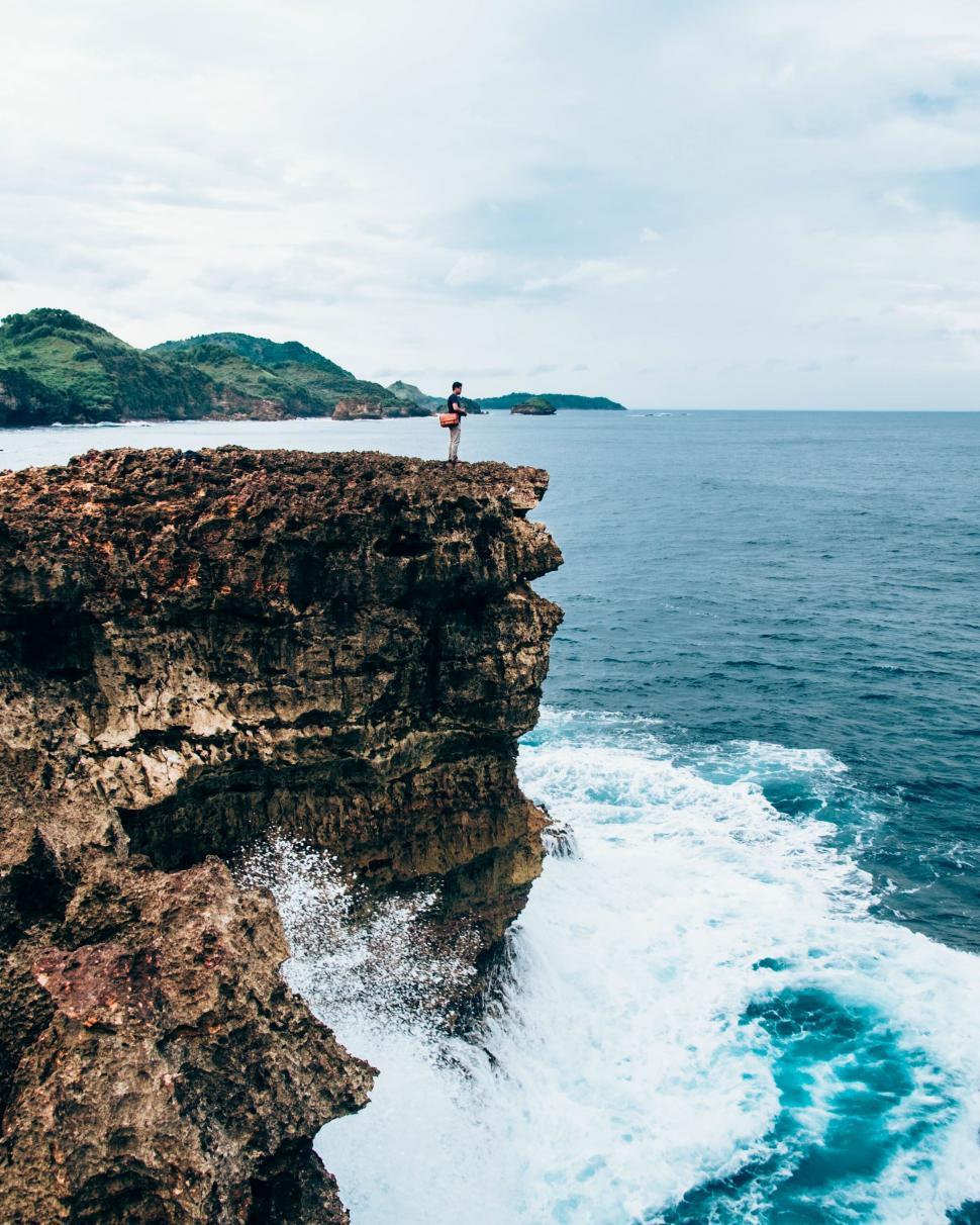 Free Image of Person standing on cliff by roaring sea 