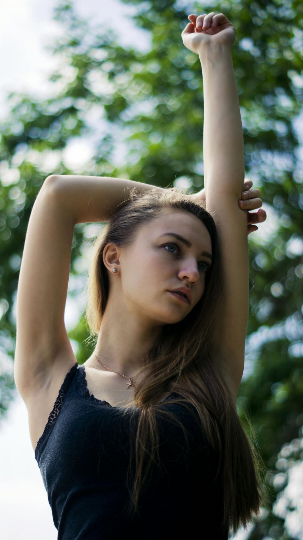 Free Image of Woman stretching arm against green foliage 