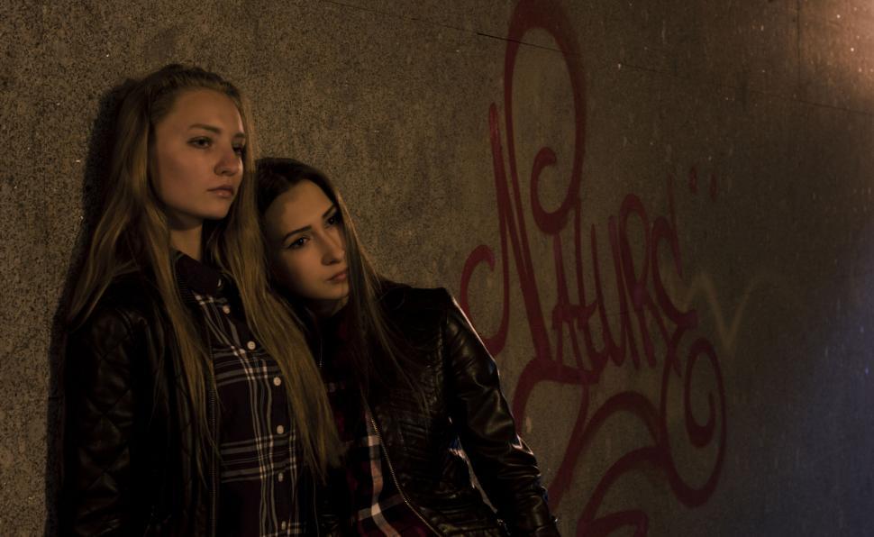 Free Image of Two women in jackets by graffiti wall at night 