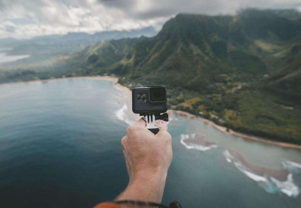 Free Image of Hand holding an action camera with coastal view 