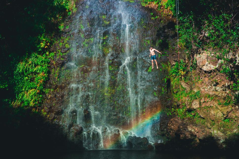Free Image of Man climbing waterfall with rainbow 